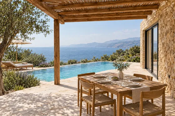 Dining table beneath a timber pergola overlooking the pool and sea.
