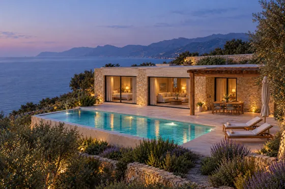 Villa and private pool at dusk, with warm interior lighting and a blue coastal horizon.